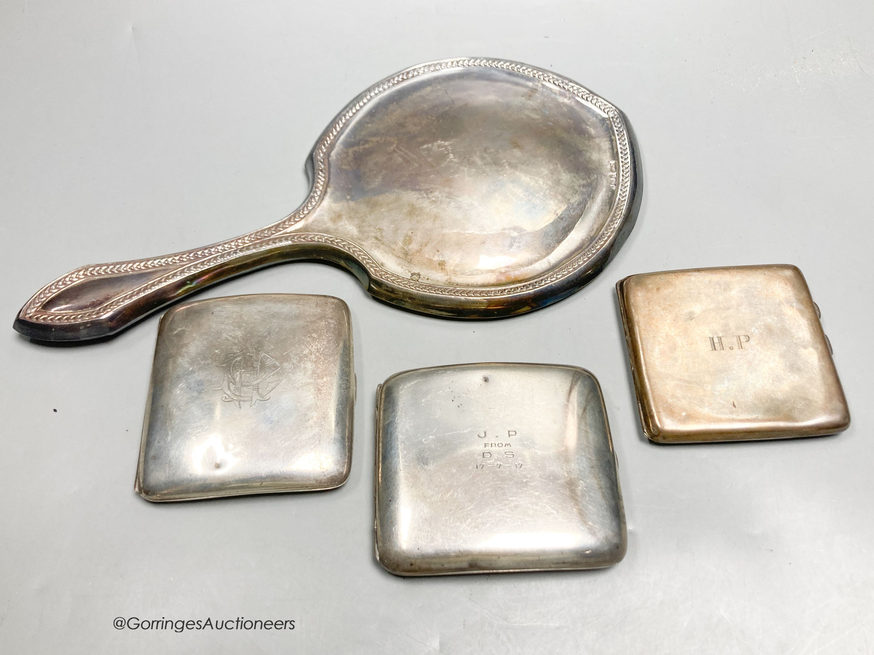 A George V silver mounted hand mirror and three silver cigarette cases.